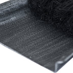 Close-up of the pan’s silver-stippled dark surface and raised edge beside dense black brush bristles.