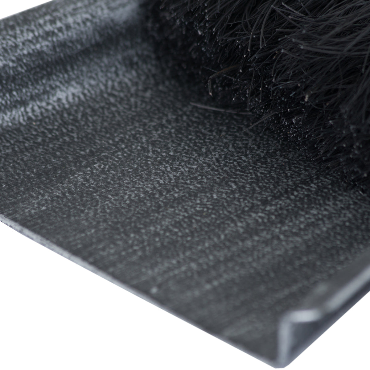 Close-up of the pan’s silver-stippled dark surface and raised edge beside dense black brush bristles.