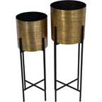 Angled view of both etched brass-coloured planters, showing their dark interiors and black cross-braced stands.