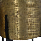 Detail of the etched rectangular pattern on a brass-coloured pot beside an upright black stand support.