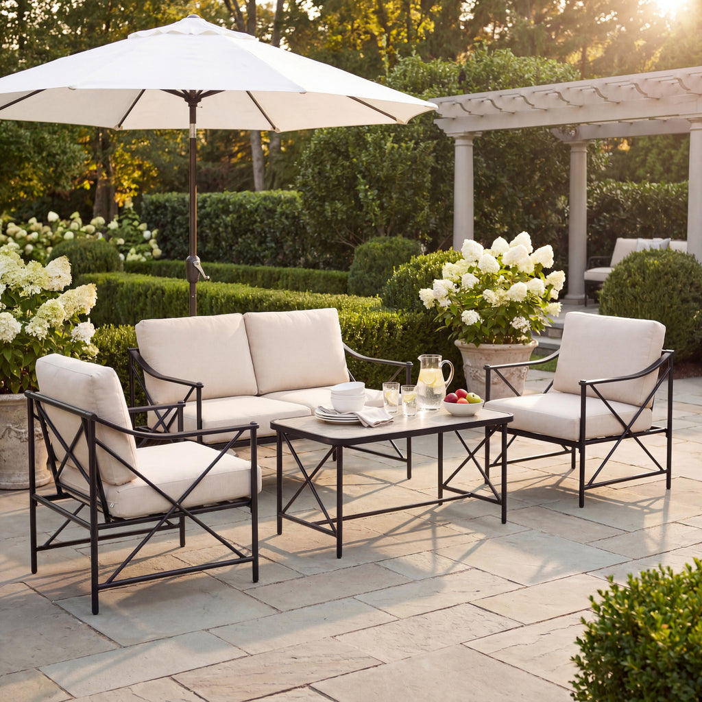 Lounge seating arranged around a table styled with tableware and a jug on a paved garden terrace beneath a white parasol.