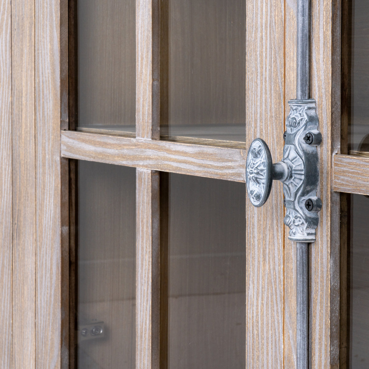 Close-up of an ornate silver-grey oval handle and vertical rod beside the door's pale brown, white-highlighted grain and cross divisions.
