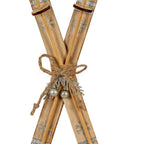 Close-up of the skis' grain-patterned surfaces, shimmering snowflakes and twine bow above a silver-coloured sprig and two rounded decorations.