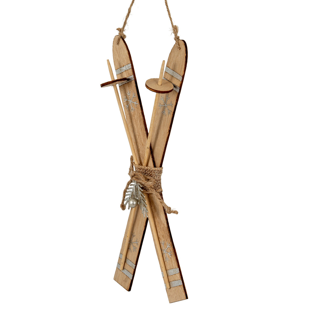 Angled view of the crossed skis showing their dark edges, slender pole forms with circular discs, and silver-coloured snowflake decoration.