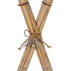 Close-up of the ski ornament's woven-looking centre band and twine bow, with a silver-coloured sprig and spherical bell-like detail below.