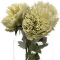 Close view of pale yellow-green artificial flowers and green leaves arranged in a clear glass vase against a white background.