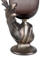 Detail of the textured metallic base with sweeping folds, an open curl and a round foot beneath the glass.