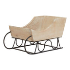 Front three-quarter view of a pale decorative sleigh with curved sides, a black frame and runners curling upwards at the front.