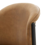 Close-up of the brown chair back's rounded top and stitched right edge beside a dark frame tube.