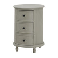 Pale grey cylindrical side table on a white background, with three curved framed drawer fronts, dark round knobs and short shaped feet.