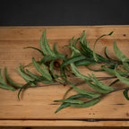 Artificial eucalyptus foliage laid across a wooden surface, showing narrow curling leaves with pale undersides and darker green upper faces.