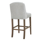 Rear three-quarter view showing the stool's broad pale grey covered back, piped upper edge and brown legs.