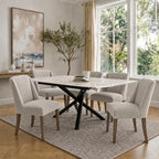 Neutral upholstered dining chairs arranged around a pale rectangular table with a black crossing base, beside large windows.