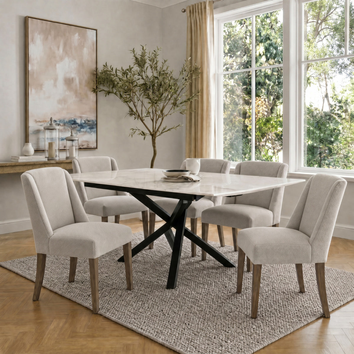 Neutral upholstered dining chairs arranged around a pale rectangular table with a black crossing base, beside large windows.