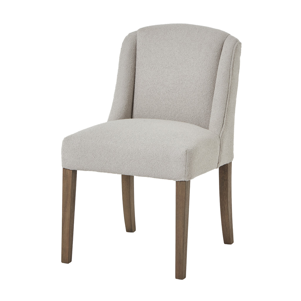 Three-quarter view of a pale upholstered dining chair with a curved wing back and four brown wooden legs on white.