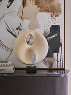 Cream cutout sculpture displayed beside stacked books on a dark console, with abstract artwork behind it.
