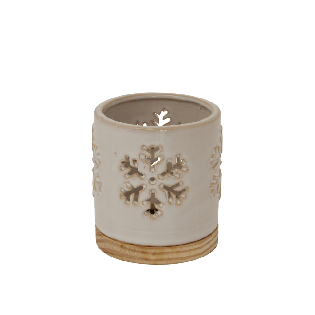 Angled view of the cream candle holder showing open snowflake cut-outs, a rounded rim and a warm-toned patterned base.