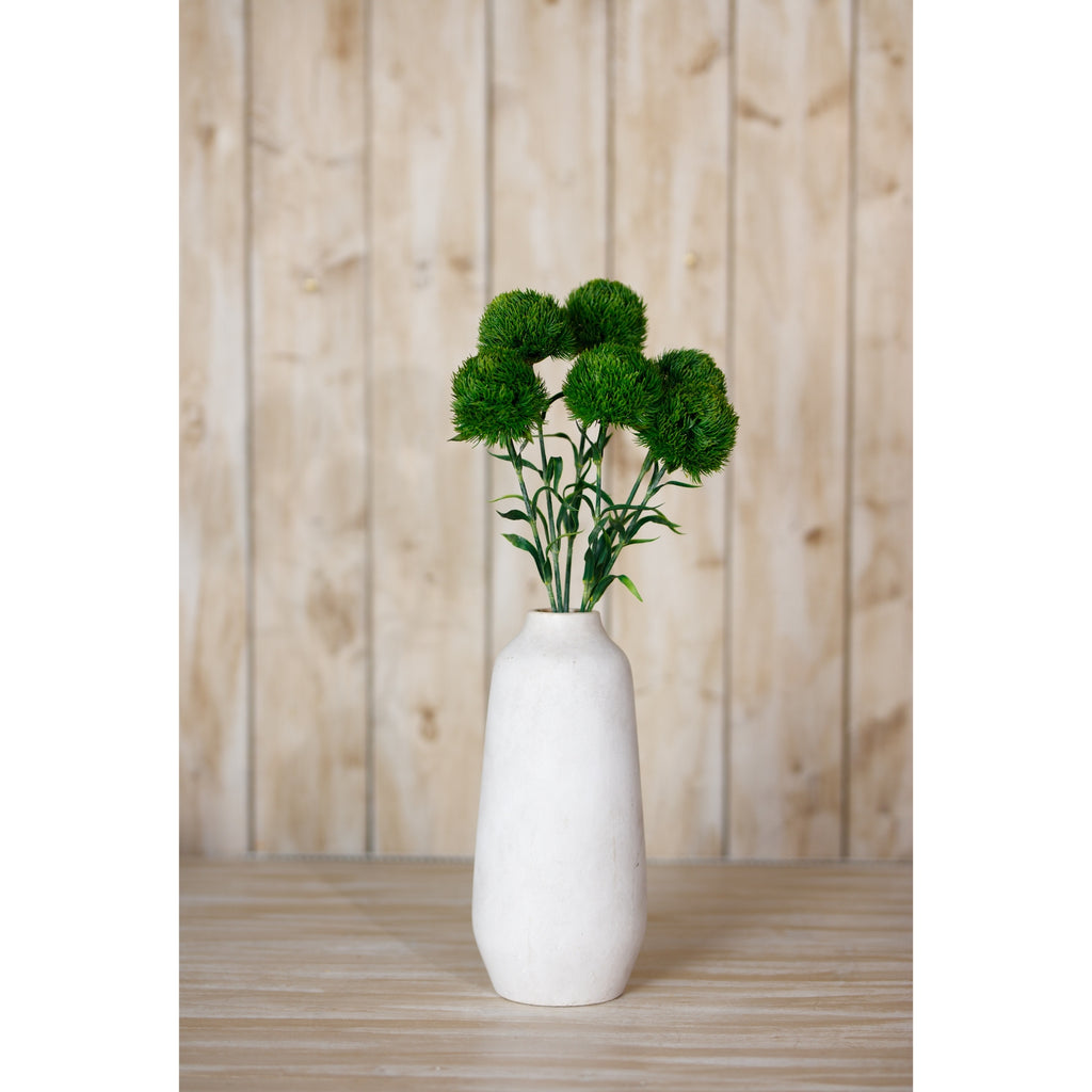 Green dianthus arrangement in a tall cream vase on a wooden surface in front of pale vertical timber boards.