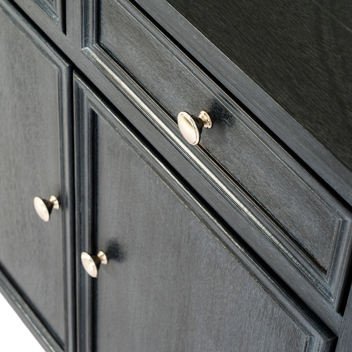 Angled close-up of the sideboard's pale round drawer knob, dark surface texture and layered panel edges, with the door knobs below.