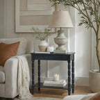 Dark turned-leg console table beside a cream sofa, styled with a pale lamp, vase and ornaments on top, and books and a glass candle on the lower shelf.