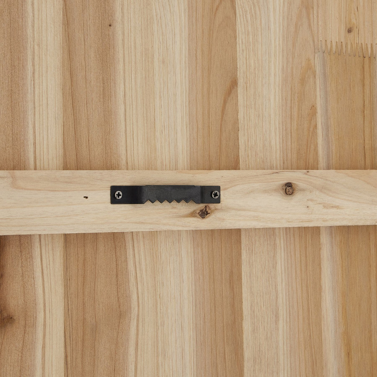 Rear close-up of the clock showing a black toothed hanger screwed to a horizontal strip across the light wood-coloured backing.