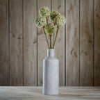Styled arrangement of five pale green and cream spherical flower heads in a tall grey vase on a wooden surface, against vertical wood panels.