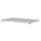 Low angled view of the serving board showing its thin pale edge, lightly marbled top and black pads beneath.