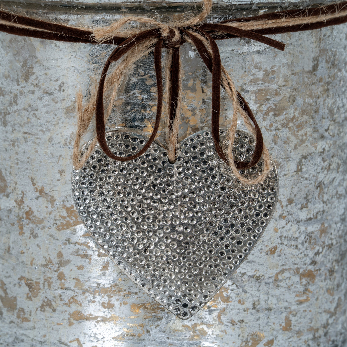 Close-up of the silver-toned heart pendant with shallow dimples, suspended beneath loops of twine and dark cord.