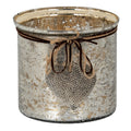 Broad cylindrical candle holder with a mottled silver and gold-toned surface, twine and dark cord bow, and hanging dimpled heart.