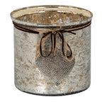 Broad cylindrical candle holder with a mottled silver and gold-toned surface, twine and dark cord bow, and hanging dimpled heart.