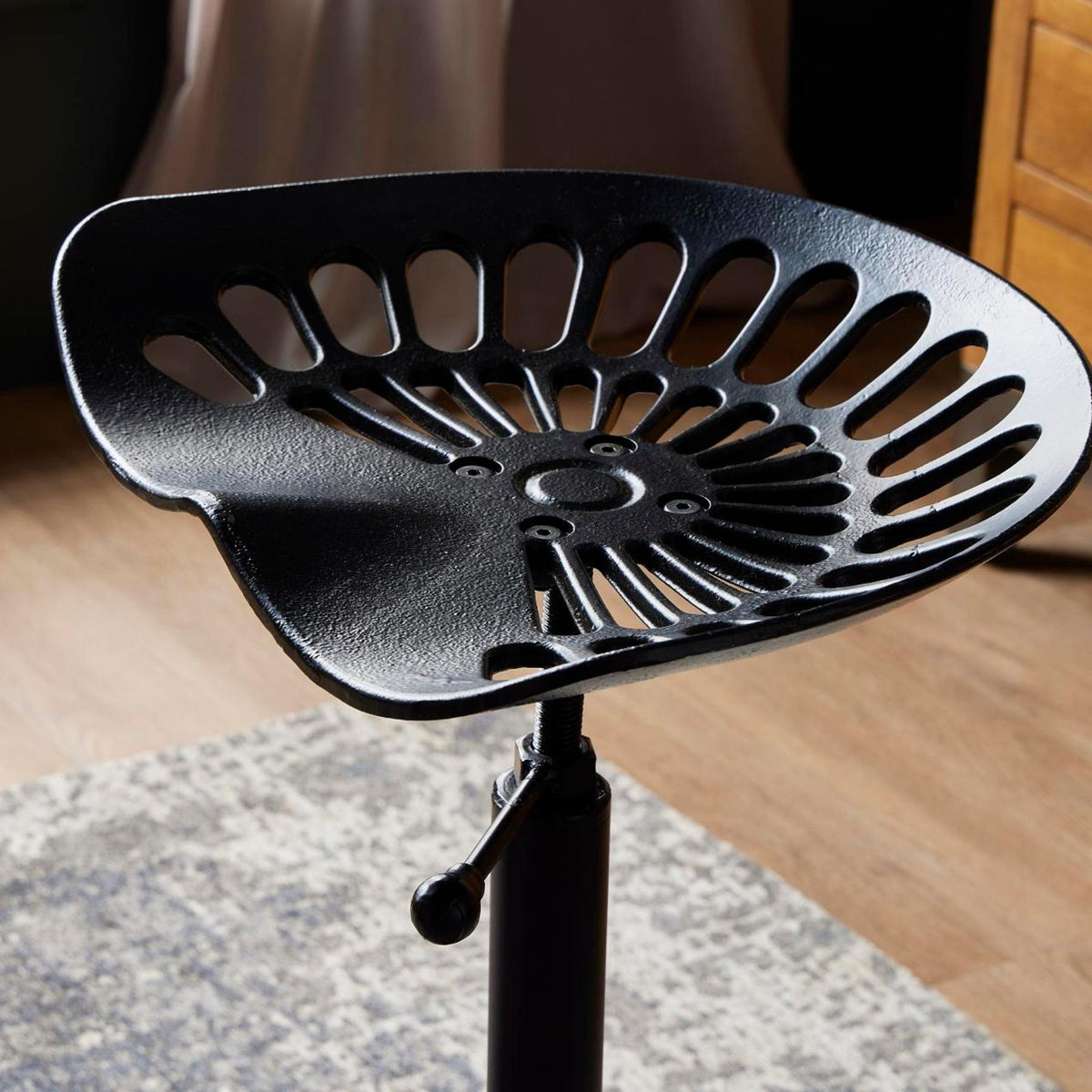 Close-up of the stool's dished black seat, with radiating oval openings, a textured surface and a handle beneath the front edge.