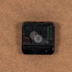 Close-up of the black clock movement on the brown back panel, with QUARTZ lettering, a setting wheel and an empty battery compartment visible.