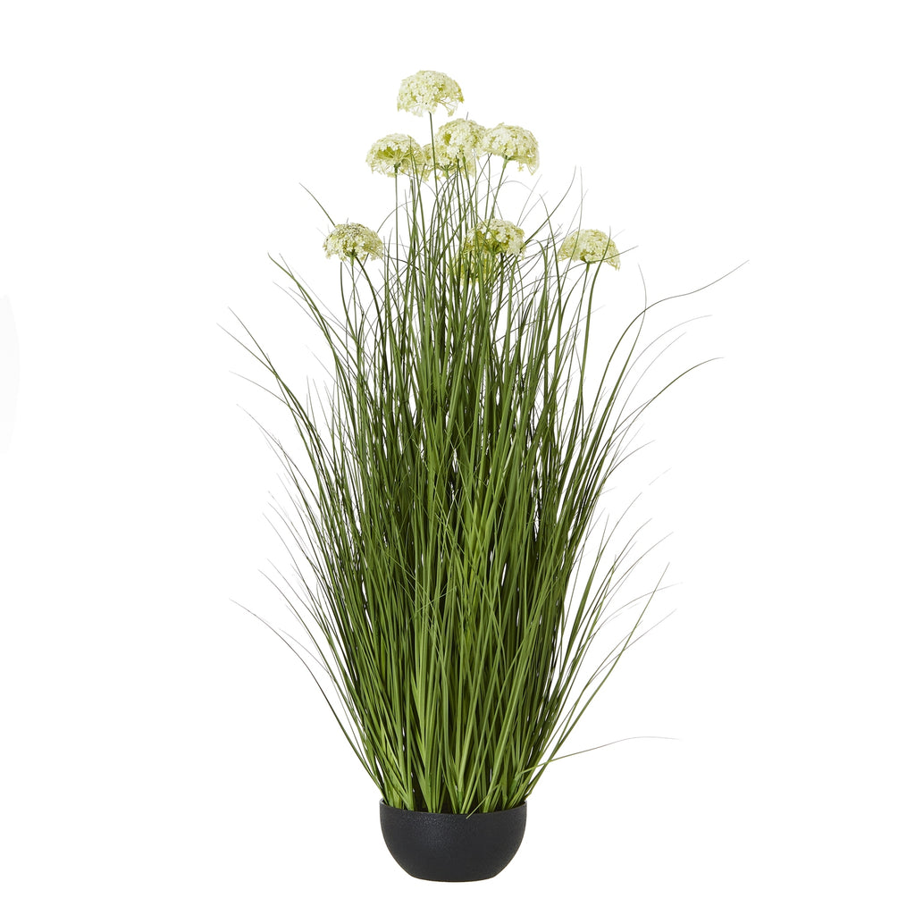 Full view of the artificial arrangement, with tall green blades and pale domed flower heads rising from a low rounded black pot.