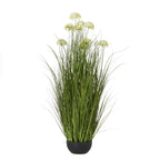 Full view of the artificial arrangement, with tall green blades and pale domed flower heads rising from a low rounded black pot.
