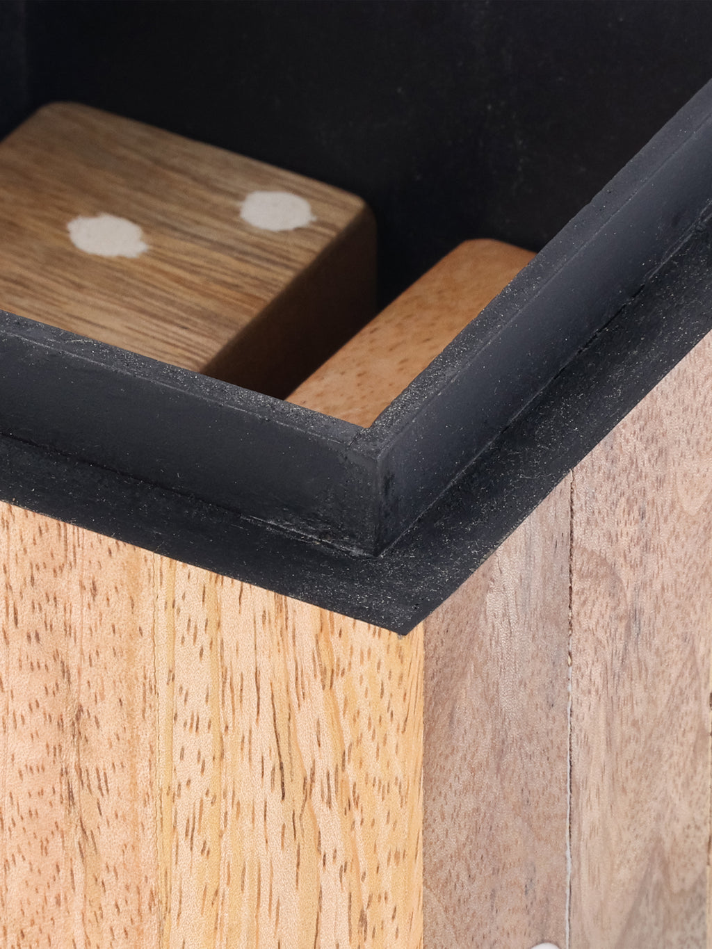 Detail of wooden dice inside the box, framed by the dark-lined rim and pale wood exterior.