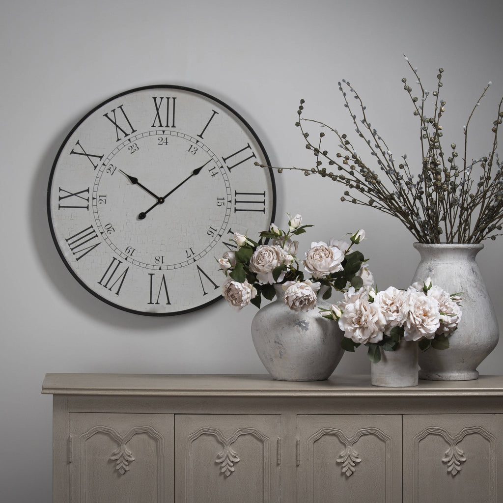 Doublehour Dial Wall Clock on a grey wall above a carved sideboard, styled beside pale vases holding flowers and tall branches.