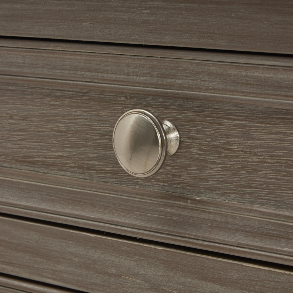 Close-up of a round silvery drawer knob against the pale streaked grey-brown finish and raised border of the drawer front.