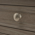 Close-up of a round silvery drawer knob against the pale streaked grey-brown finish and raised border of the drawer front.