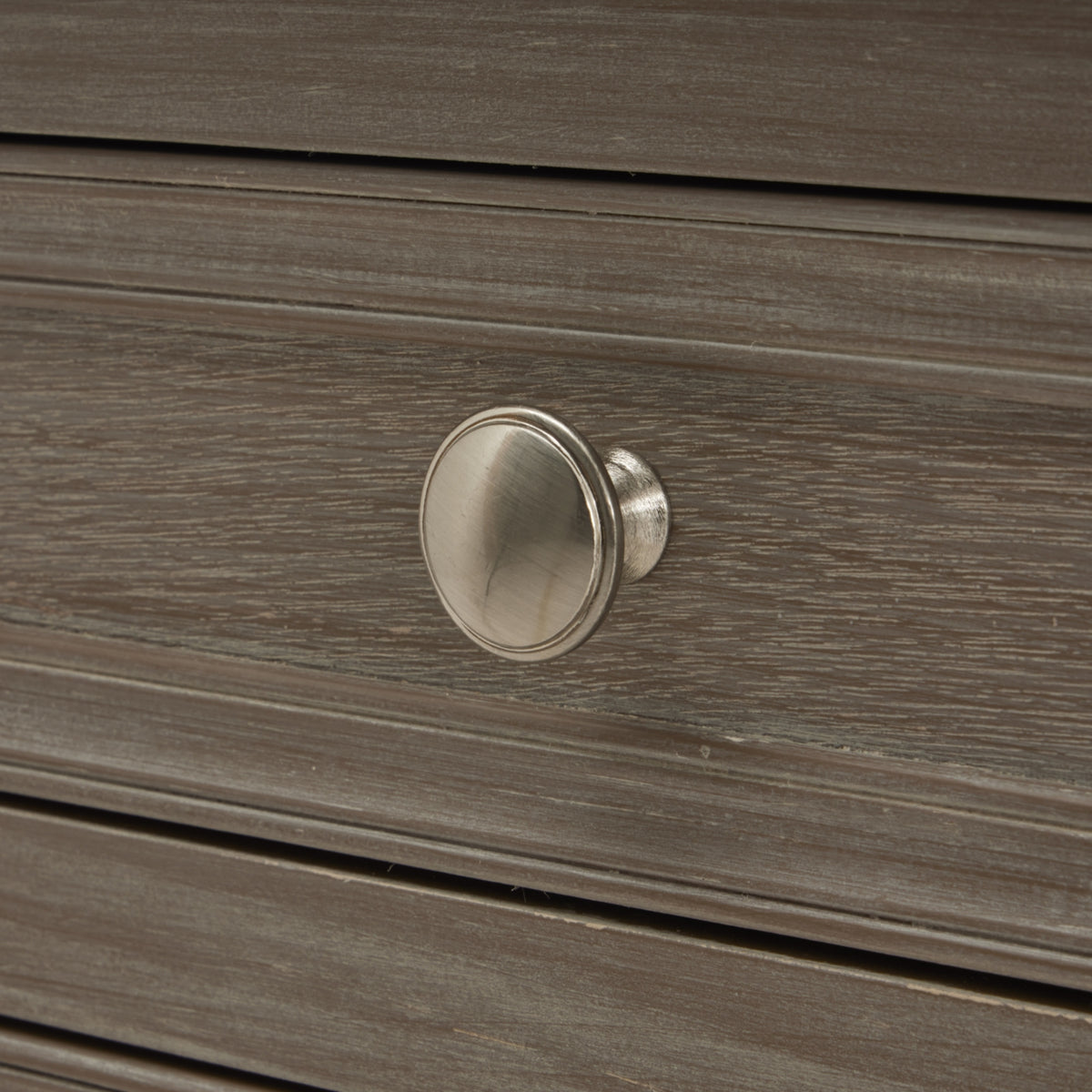 Close-up of a round silvery drawer knob against the pale streaked grey-brown finish and raised border of the drawer front.