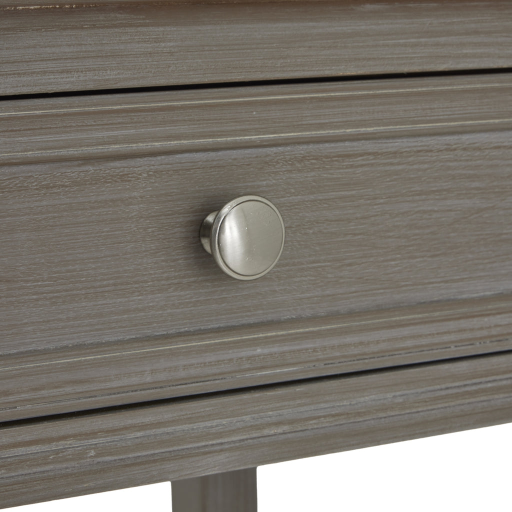 Close-up of a round silver-toned knob centred on a grey-washed drawer front with a rectangular moulded border.