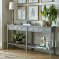 Grey-washed four-drawer console beneath framed botanical prints, styled with a lamp, vases, foliage and books across the top and lower shelves.