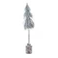 Full view of a narrow snow-effect tree decoration with drooping green fronds, a long dark trunk and cones on a cylindrical log-style base.