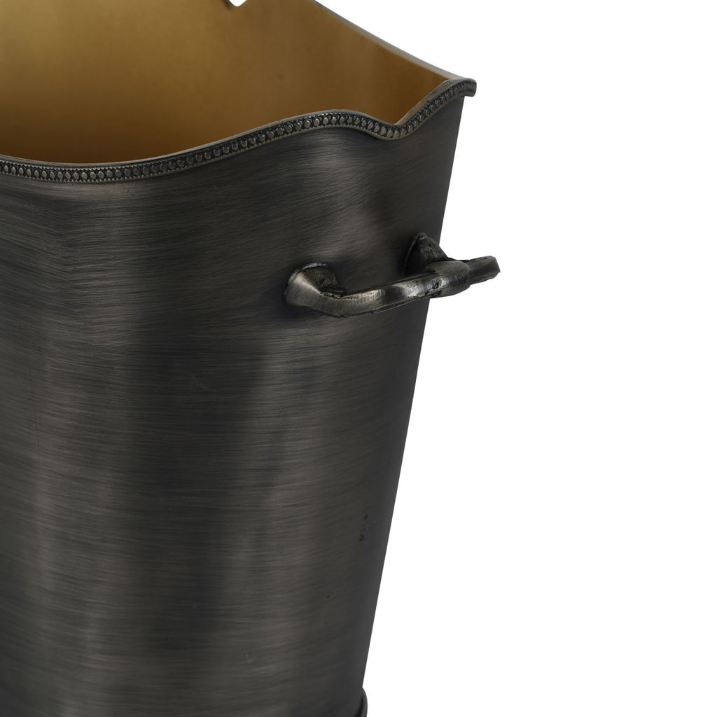 Detail of a curved side handle beneath the beaded rim, with the golden interior visible above the dark brushed exterior.