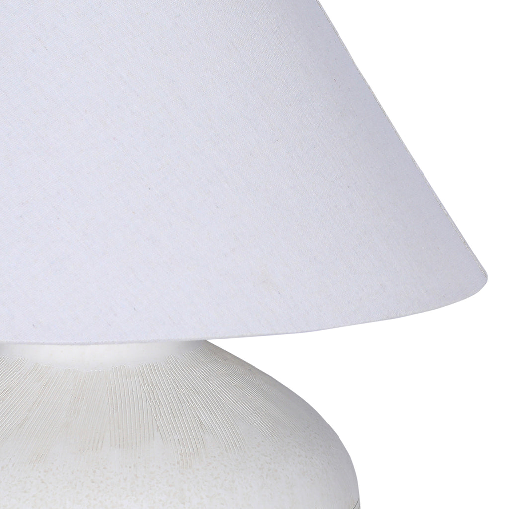 Detail of the pale fabric shade's woven surface and curved lower edge above the etched shoulder of the ceramic base.