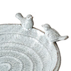 Angled close-up of both facing birds on the rim, showing the glossy pale surface, dark flecks and broad curved basin.