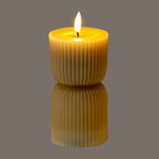 Ribbed hourglass LED candle photographed illuminated against a grey background, with yellow light around the recessed top and a bright flame-shaped element.