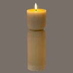 Beige ribbed LED candle photographed against a grey background, with its flame-shaped element appearing bright white and a golden glow around the recessed top.
