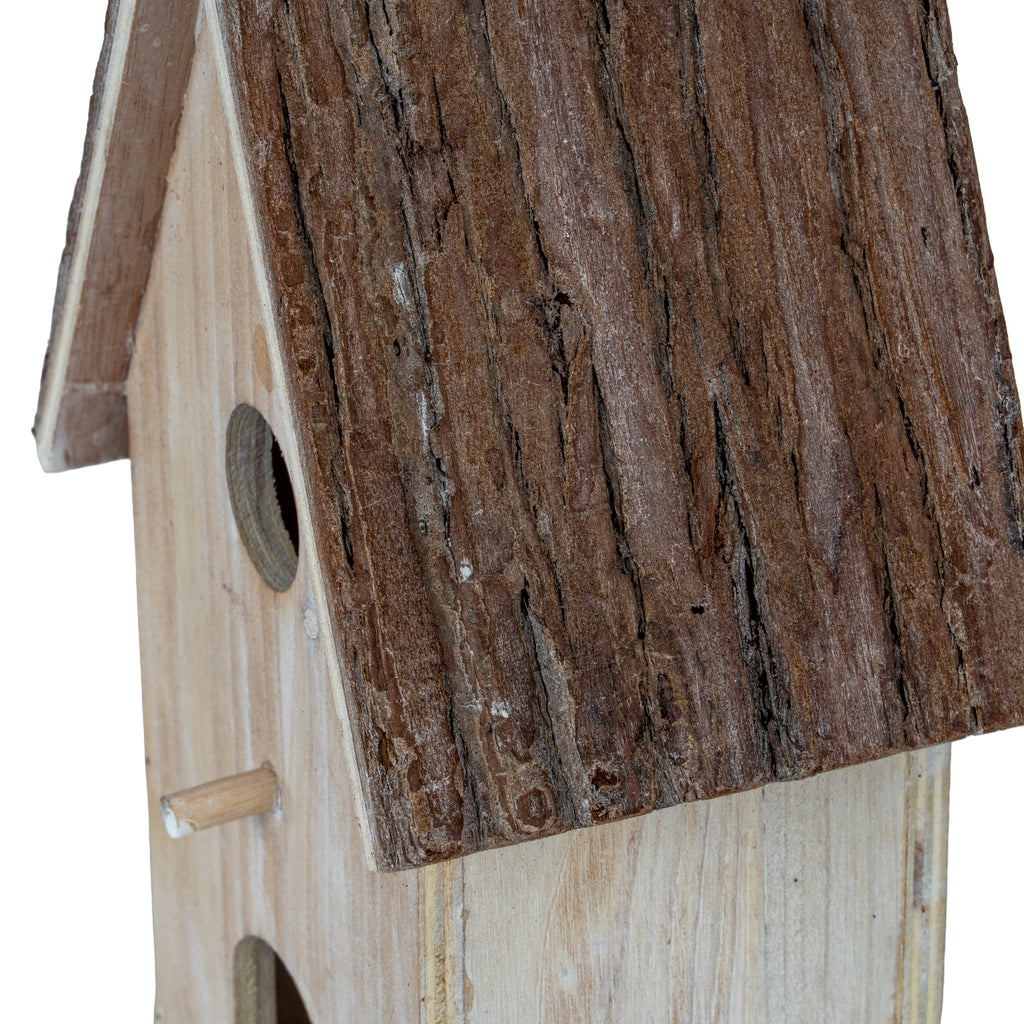 Close-up of the roof's grooved, bark-like brown texture beside the pale birdhouse front, with part of the circular opening and dowel visible.