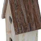 Close-up of the roof's grooved, bark-like brown texture beside the pale birdhouse front, with part of the circular opening and dowel visible.