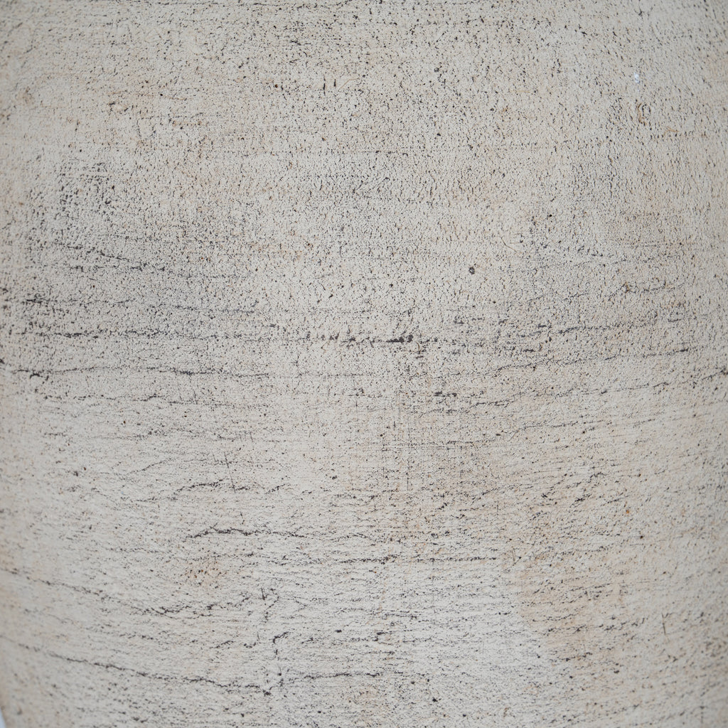 Detail of the vase's granular cream surface with tiny dark flecks and closely spaced horizontal scrape-like lines.